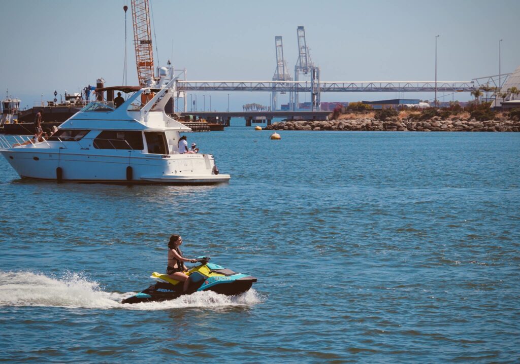 Recreational scene in Long Beach Harbor with a jet ski and yacht under a sunny sky.